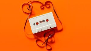 Weiße Audiokassette mit herausgezogenem Band auf orangefarbenem Grund