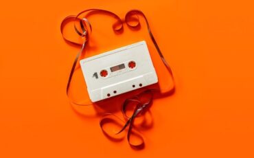 Weiße Audiokassette mit herausgezogenem Band auf orangefarbenem Grund