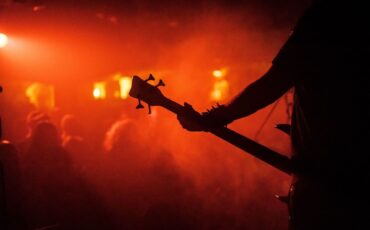 Silhouette eines Bassisten vor rot-orange beleuchteter Konzertbühne