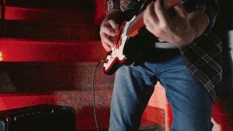 Nahaufnahme eines Gitarristen mit E-Gitarre vor rot beleuchtetem Verstärker